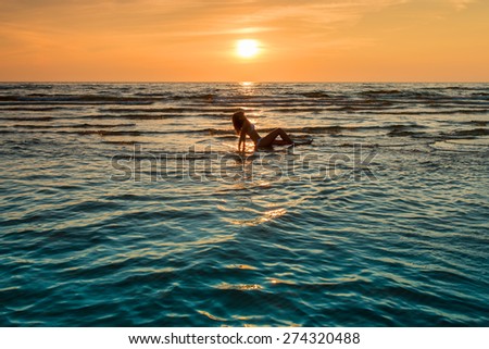 woman in white bikini posing in a sea at sunset time