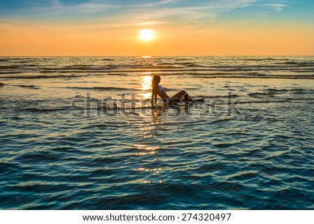 woman in white bikini posing in a sea at sunset time