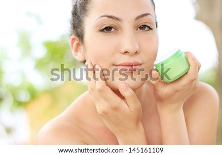 Woman applying moisturizer cream on face. Close-up fresh woman face