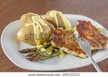 Green Asparagus with potatoes, pork and hollandaise sauce on a white plate