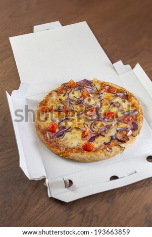Delivered pizza with tomatoes and onions in a open pizza box on a brown wooden table