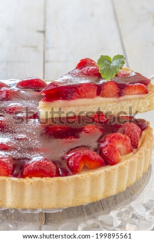 Homemade strawberry cake with one slice lifted up on a glass platter on a wooden table