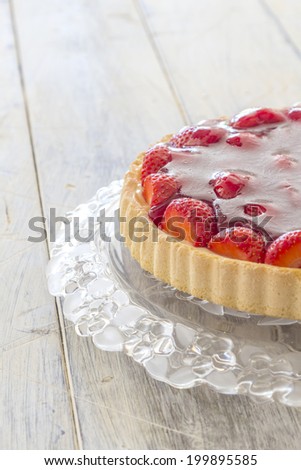 Homemade strawberry cake on a glass platter on a wooden table