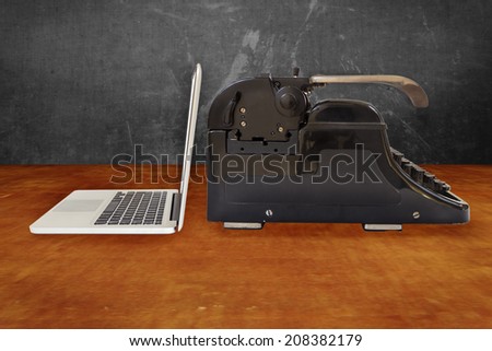 Modern silver laptop and an old black typewriter on a wooden table