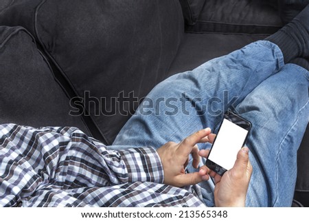 Man in checkered shirt relaxing on a couch surfing on a smartphone with white isolated screen