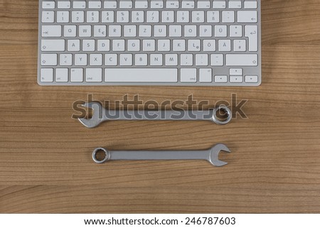 Modern keyboard and two wrenches on a wooden Desktop