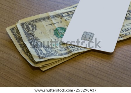 A Blank white Credit or Debit Card and a couple of dollar notes on a wooden table