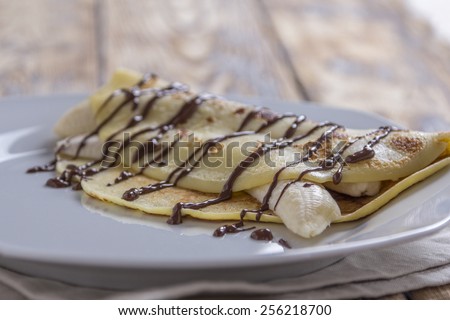 crepe filled with banana and chocolate sauce topping on a rustic wooden plate