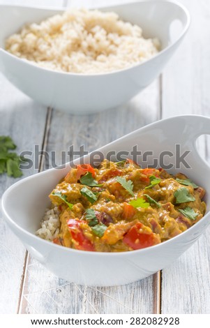 chicken curry, red pepper and coriander leaves with rice in a white bowl