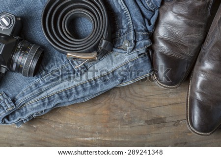 Jeans, Belt, leather boots and vintage camera on a rustic wooden background