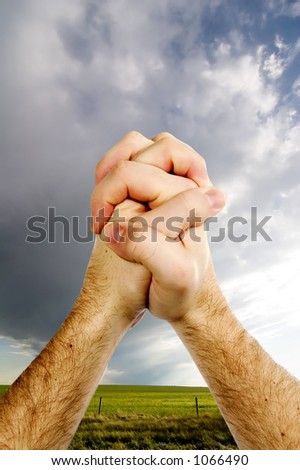 A pair of hands praying with a prairie landscape with rain clouds in the background.