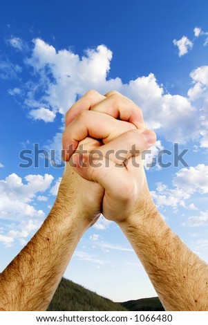 Praying hands on top of a beautiful prairie landscape with a deep blue sky and picturesque clouds.