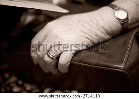 A detail of an old womans hand on her purse using shallow depth of field. The image is given a slight sepia toning
