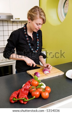 A woman cutting red onions at home on the counter - preparing to make a pizza with tomatoes and peppers.