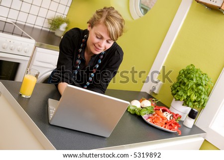 A young woman using the computer while eating a healthy snack in an apartment kitchen;