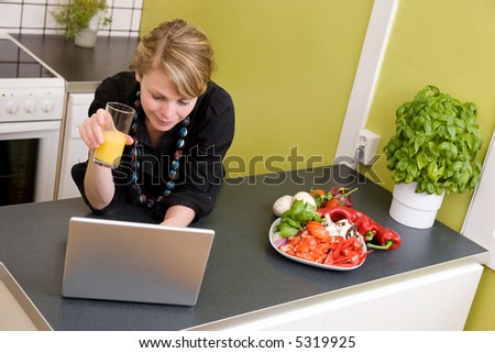 A young female surfs the internet while enjoying a light healthy snack of vegetables and juice.