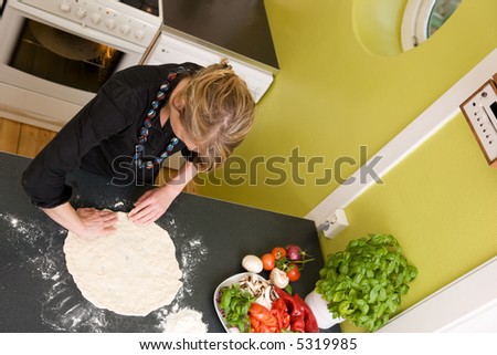 A young woman is making pizza dough on the kitchen counter at home in her apartment - viewed from above.