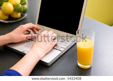 A computer in the kitchen with a female hand using the touch pad.  The laptop has a completely black screen for easy editing.