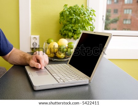 A computer in the kitchen with a male hand using the touch pad.  The laptop has a completely black screen for easy editing.