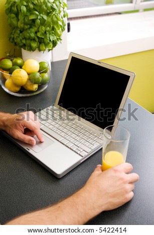 A computer in the kitchen with a male hand using the touch pad.  The laptop has a completely black screen for easy editing.