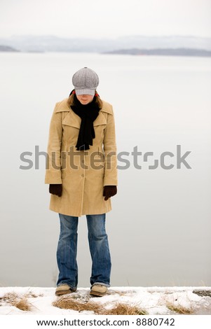 A young woman standing by the ocean in winter with head down