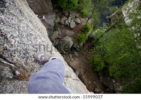 A foot on a ledge of a very high rock face