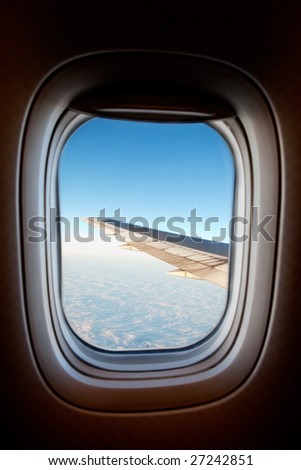 An airplane window with wing and cloudscape