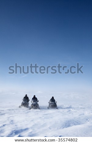 Three snowmobiles on a winter landscape with blowing snow
