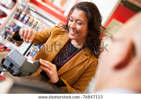Shop assistant smiling while swiping credit card in supermarket with customer in the foreground