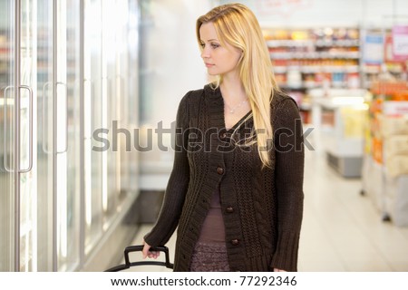 Young woman looking at goods in refrigerator section of supermarket