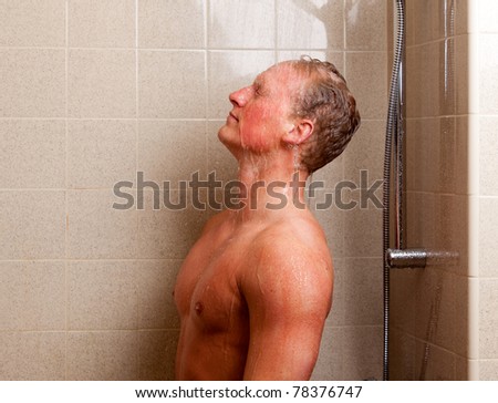 Torso of a man showering with head back, water on face