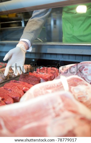 A hand showing the various meat options at a fresh meat counter