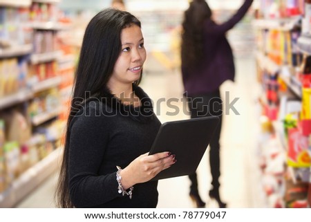 Young woman looking at the products while using digital tablet in shopping centre with person in the background