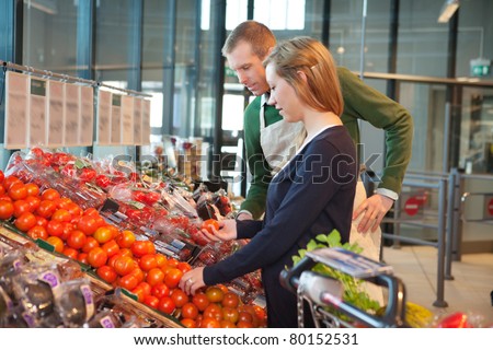 Woman holding tomato while standing with shop worker in grocery store