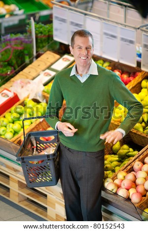Mid adult man carrying shopping basket and looking at camera while shopping in fruit store