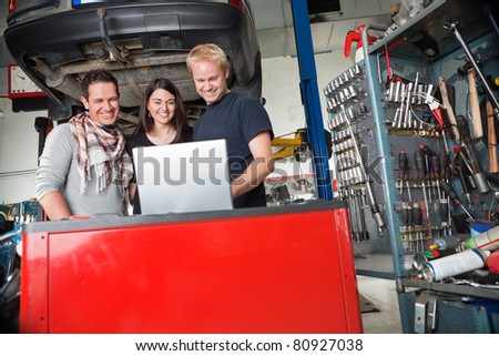 Young smiling couple standing with mechanic using laptop in auto repair shop