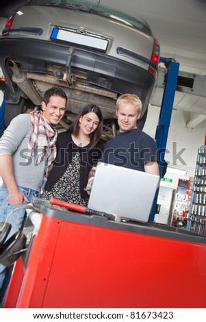 Smiling young couple standing with mechanic using laptop in auto repair shop