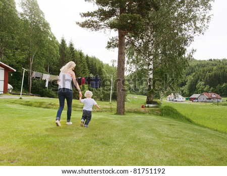 Rear view young woman and son holding hands in garden and walking