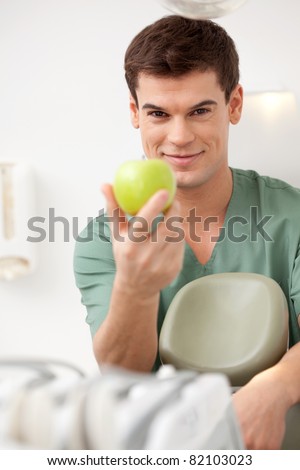 A happy young male dentist holding an apple.  Shallow depth of field, focus on dentist.
