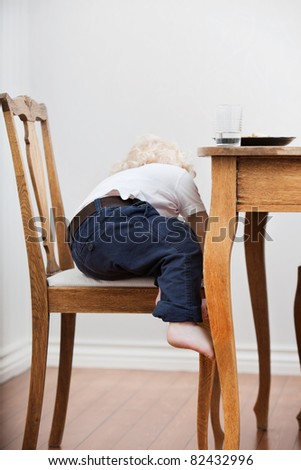 Cute blond child trying to get down from chair near dining table