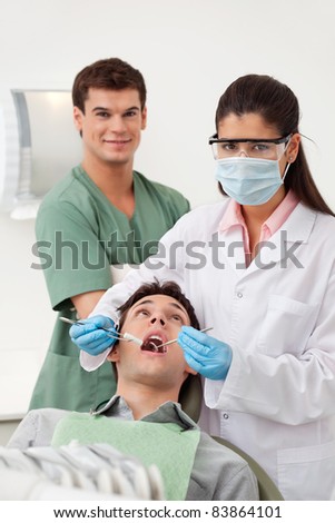Female dentist examining man\'s teeth in dental office with assistant behind