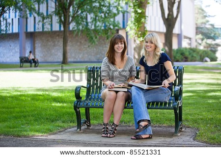 Young female students sitting on a bench on college campus