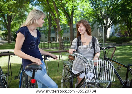 Happy young female students standing with bicycle at college campus lawn