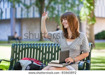 Young smiling college girl waving hand to person outside of image