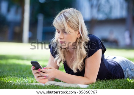 Young college girl using cell phone while lying on grass