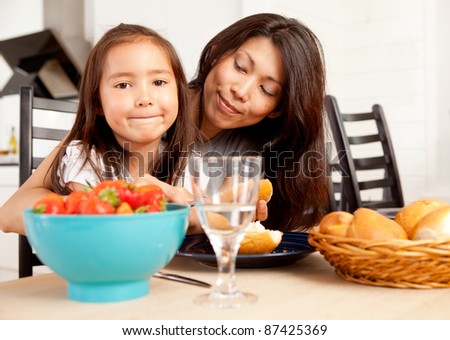Happy mother and daughter in kitchen eating meal with fresh picked strawberries