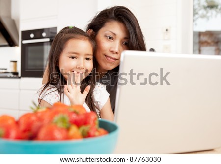 Mother and daughter using computer, waving while in a live video chat