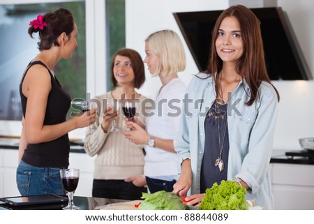 Portrait of pretty female cutting vegetables while her friends having drink in background