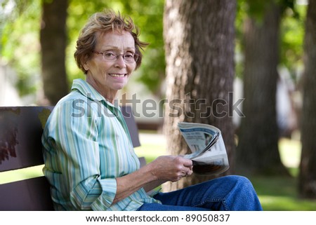 Portrait of smiling elderly woman reading newspaper in park