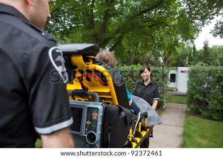 Two ambulance workers pushing elderly patient to vehicle